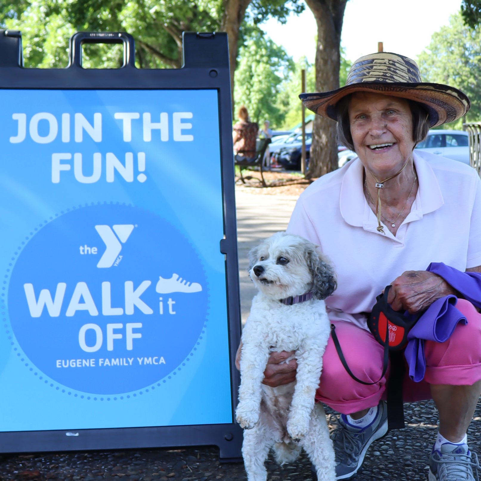 older woman poses with her dog in front of a walk it off sign