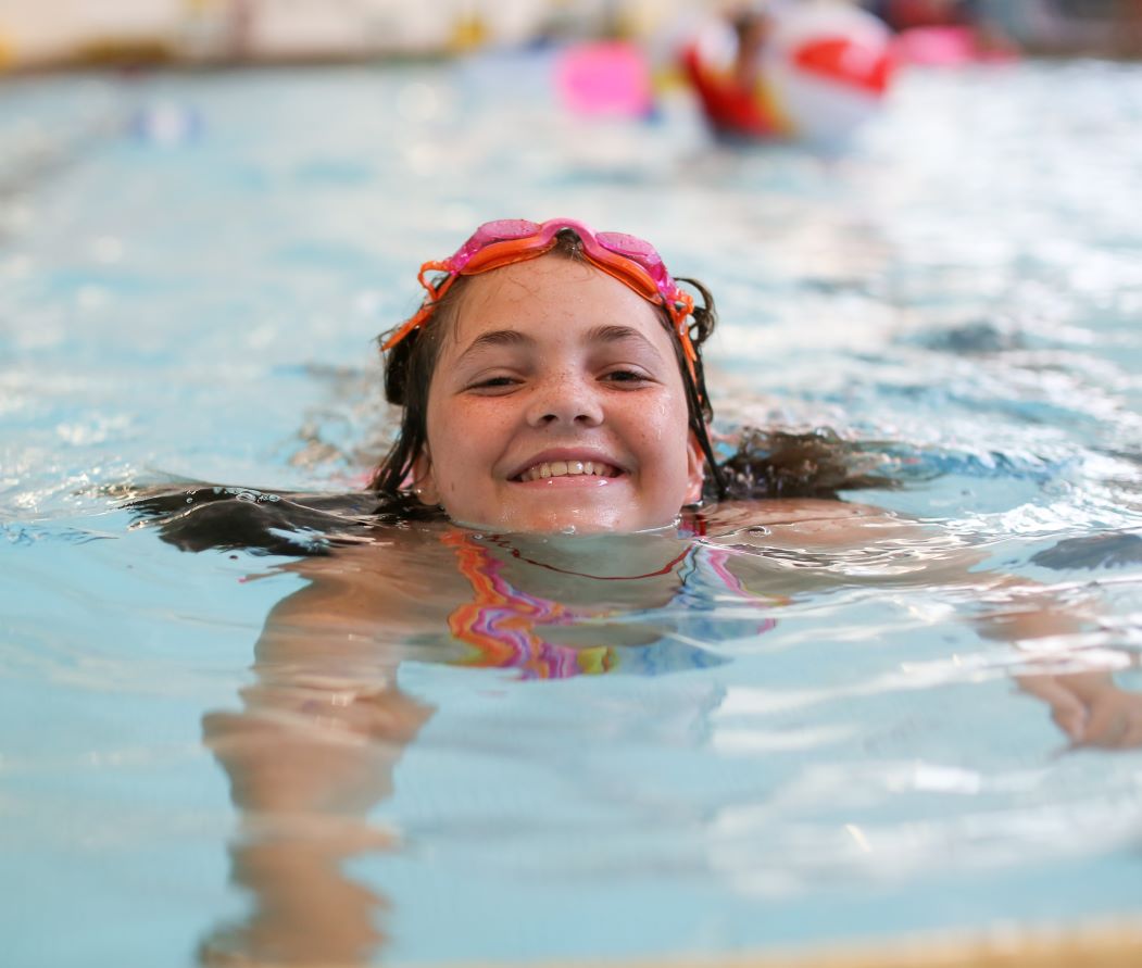 young girl smiles while swimming in the eugene ymca aquatics center