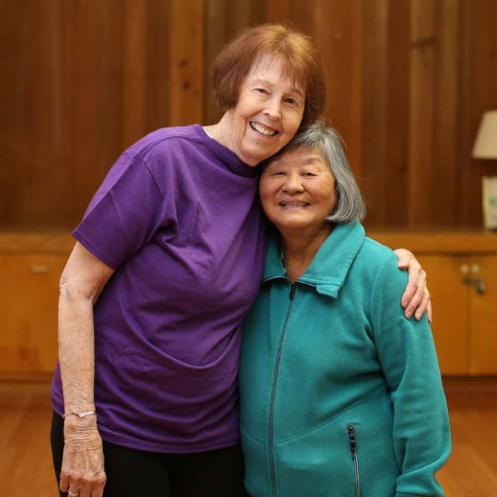 two senior women hug and smile in the eugene ymca yoga room