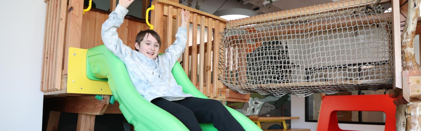 young boy goes down slide on indoor play structure in kid zone