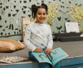 girl reads book and smiles at eugene ymca playcare