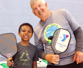 two generations of Y members holding pickleball paddles in the gym