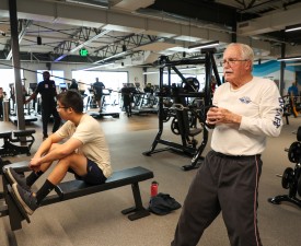 person rests on workout bench between sets, older man uses cable machine