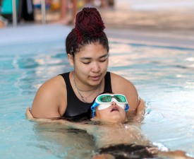 Y staff teaching a child to float on their back in swim lessons