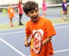 young boy smiles as he plays tennis at eugene ymca tennis center