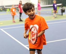 young boy smiles as he plays tennis at eugene ymca tennis center
